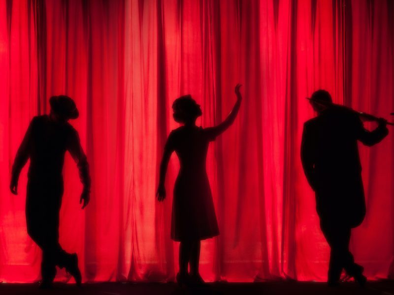 performers in the shadows on stage with a red curtain in the background